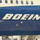 Close-up of a Boeing airplane fuselage featuring the white BOEING logo on a dark blue body with passenger windows above.