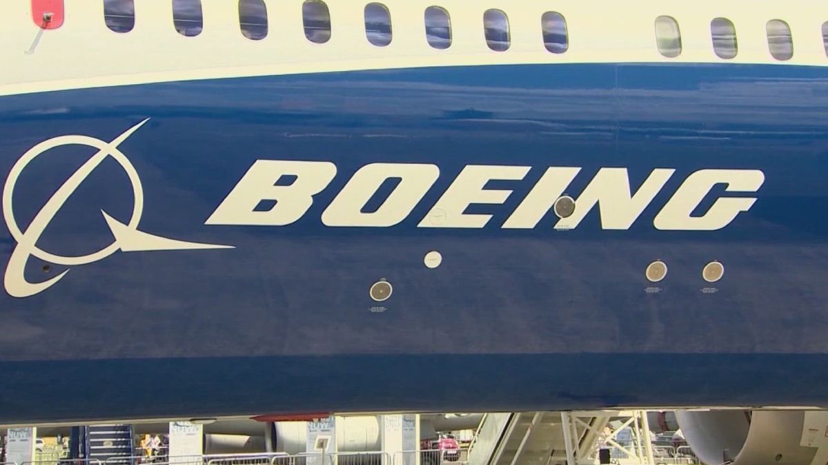 Close-up of a Boeing airplane fuselage featuring the white BOEING logo on a dark blue body with passenger windows above.