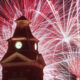 Clock tower at night with colorful fireworks bursting behind it.