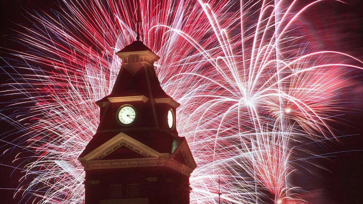 Clock tower at night with colorful fireworks bursting behind it.