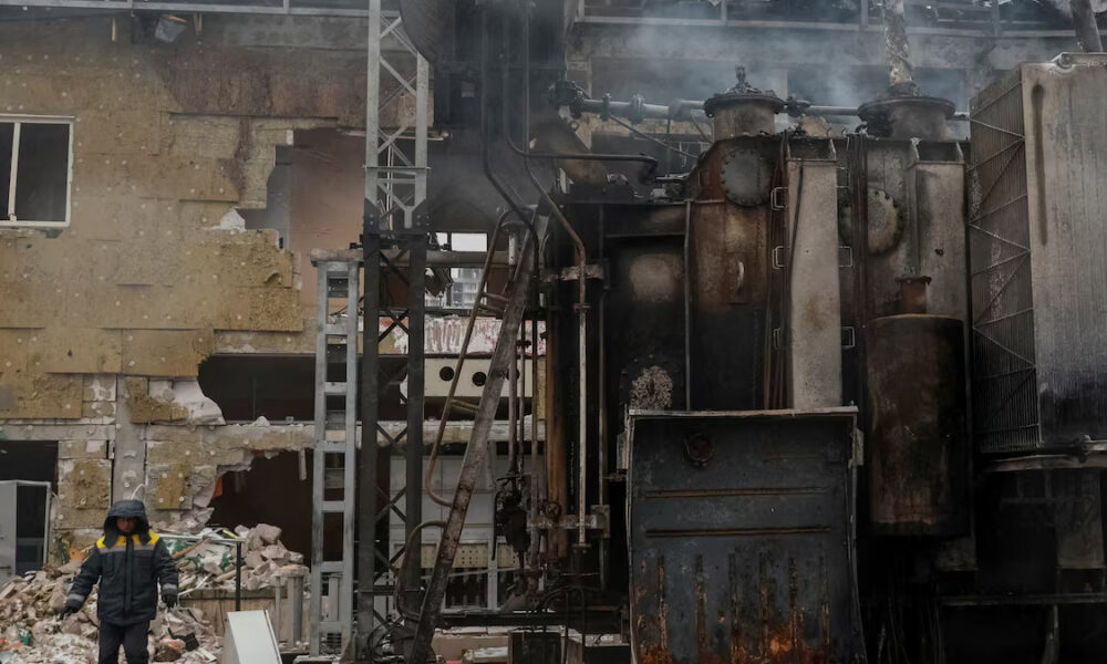 Worker in protective jacket stands beside rusty industrial machinery in a ruined factory building.