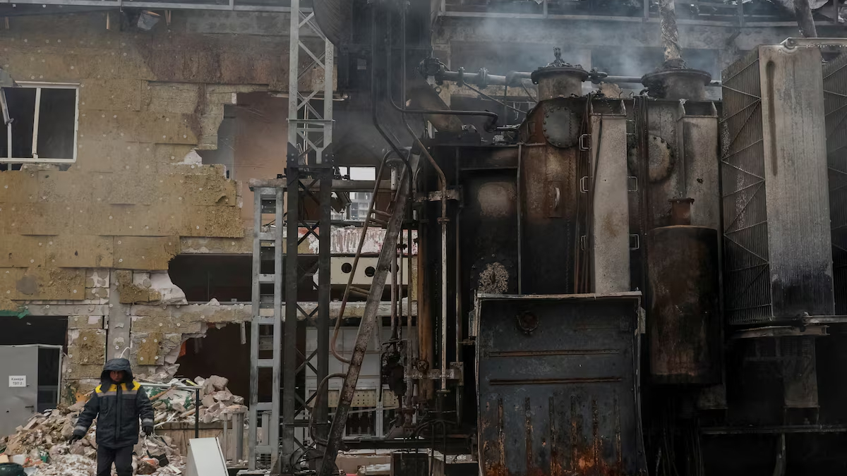 Worker in protective jacket stands beside rusty industrial machinery in a ruined factory building.
