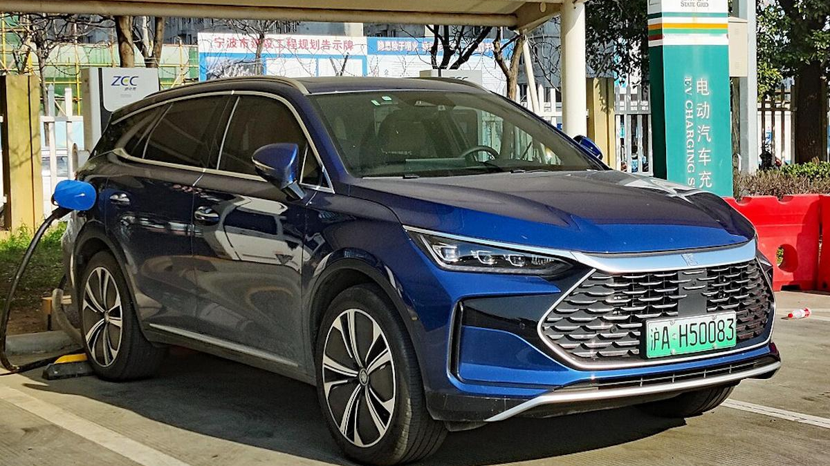 Blue electric SUV being charged at a station, front three-quarters view in a parking lot with a green license plate in Chinese characters.
