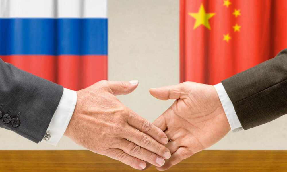 Handshake between two people in front of Russia and China flags, symbolizing international diplomacy and agreement.