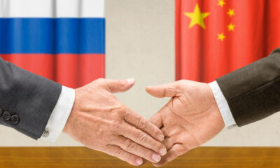 Handshake between two people in front of Russia and China flags, symbolizing international diplomacy and agreement.