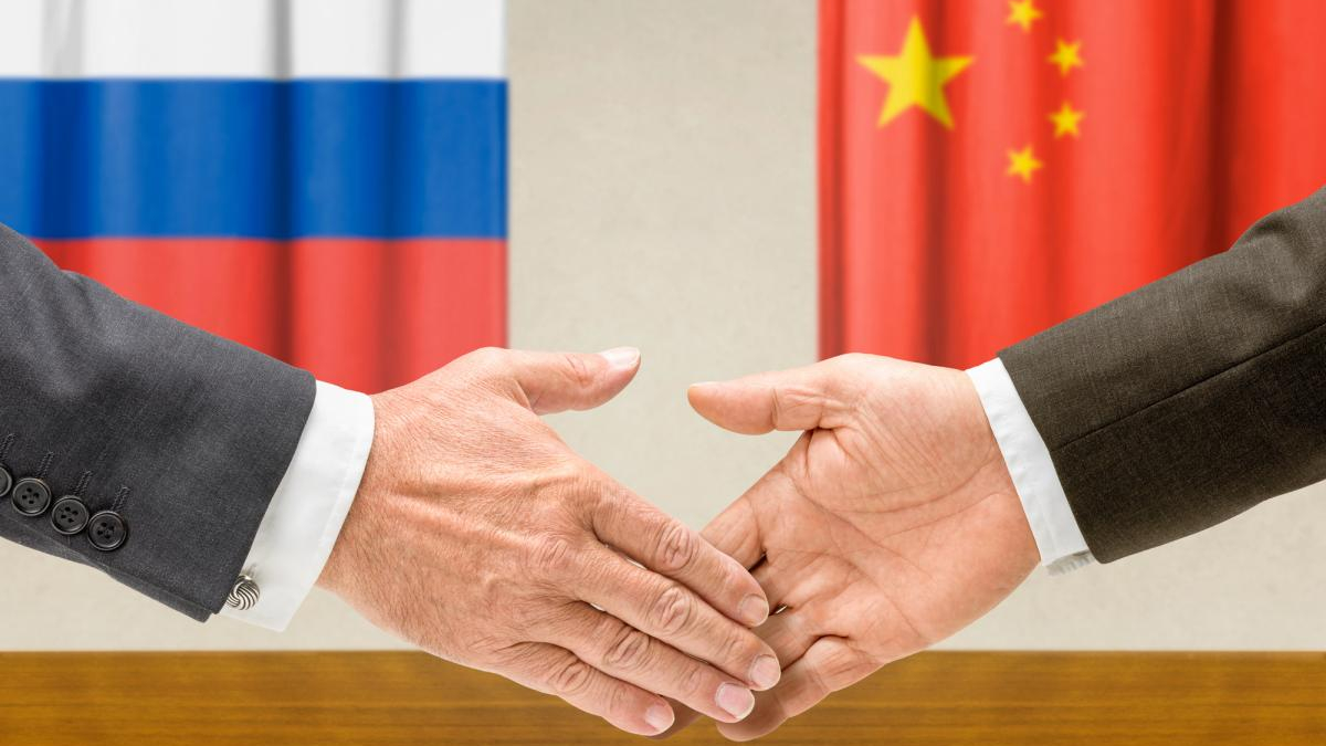 Handshake between two people in front of Russia and China flags, symbolizing international diplomacy and agreement.