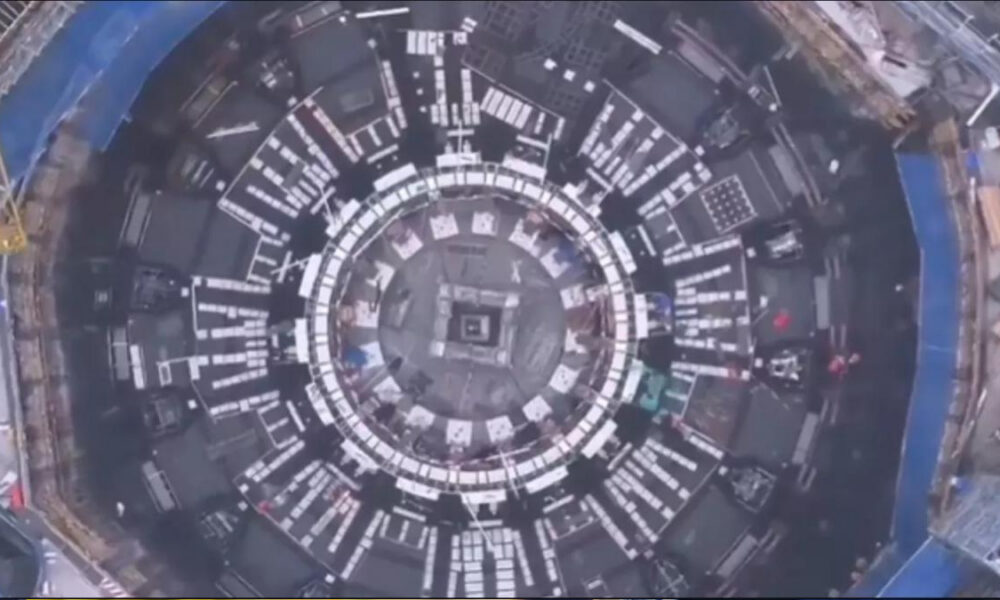 A top-down view of a large circular construction site with concentric rings and white panel modules around the ring.