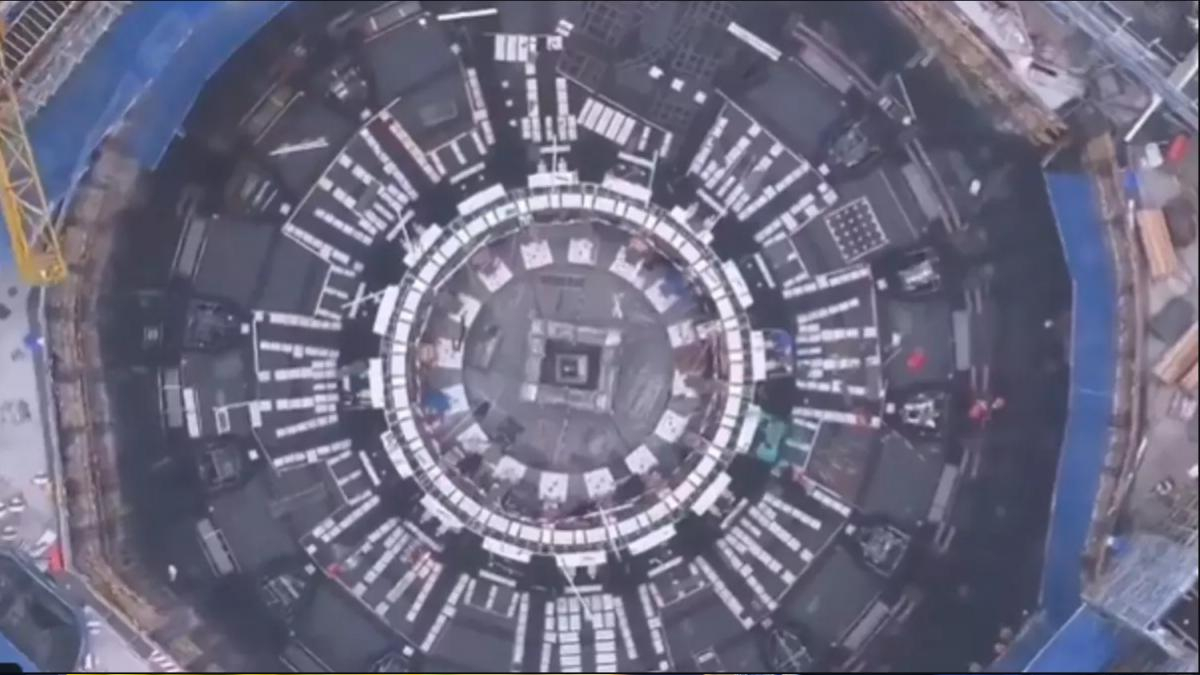 A top-down view of a large circular construction site with concentric rings and white panel modules around the ring.