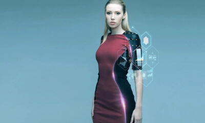 Woman in a color-block burgundy and black dress stands against a blue gradient, with holographic UI elements projected near her right arm.