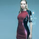 Woman in a color-block burgundy and black dress stands against a blue gradient, with holographic UI elements projected near her right arm.