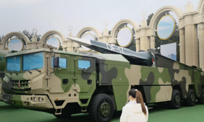 Camouflage military missile launcher truck on display with a mounted rocket and a spectator in foreground.