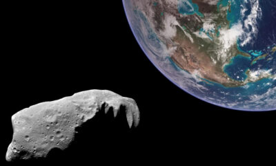 Cratered asteroid in foreground with Earth visible in the upper-right, space around.