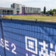 Blue construction fence banner reading 'SHS Phase 2' with a modern building and active construction equipment in the background.