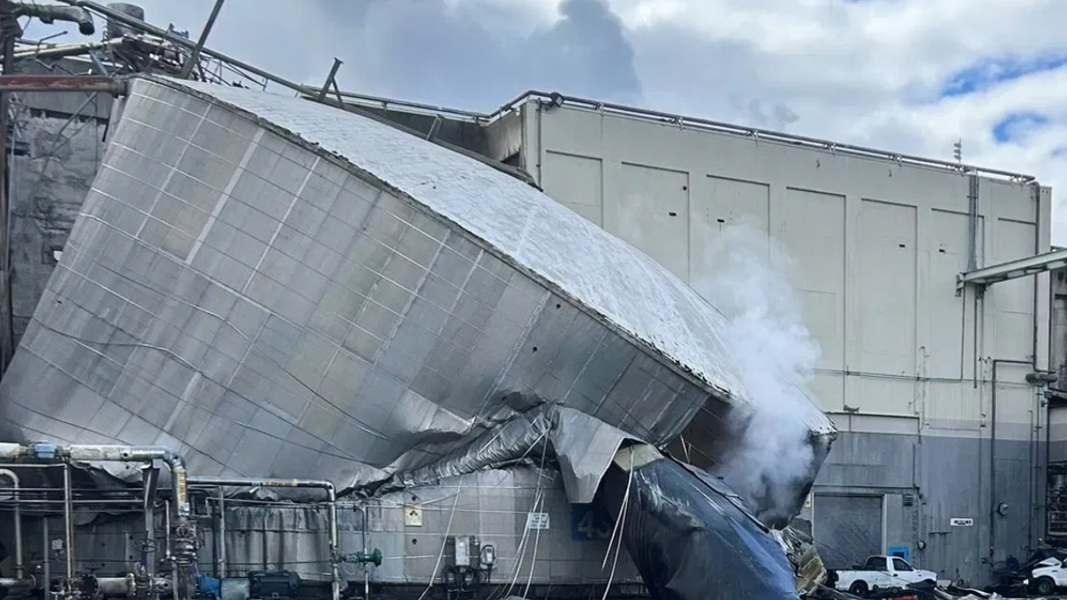 Collapsed large metallic ductwork leaning against a building after an industrial accident, with steam or smoke nearby.