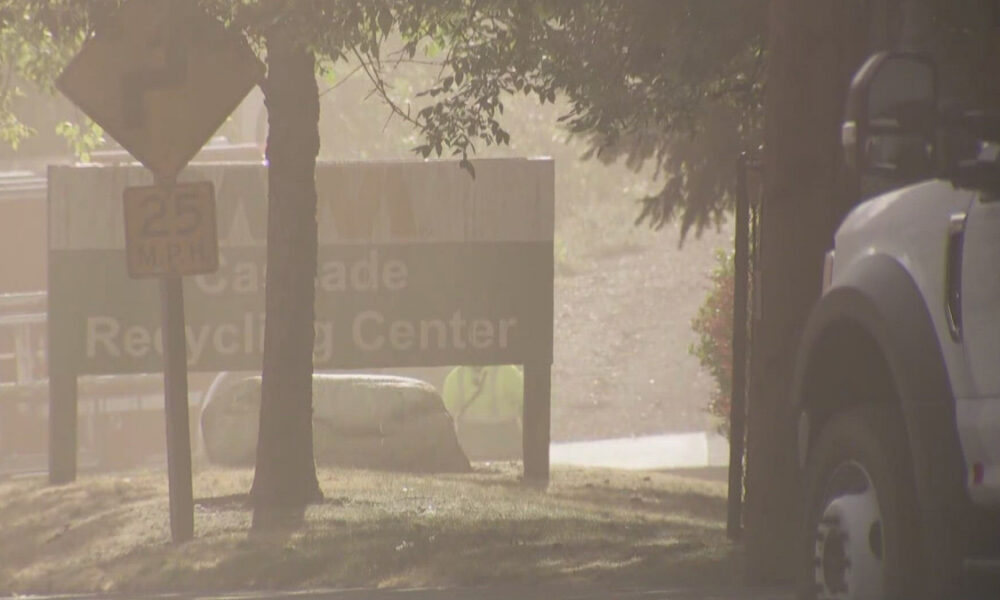 Dusty outdoor scene with a white truck on the right; foreground signs include a 25 mph sign and a 'Recycling Center' sign partially visible behind a tree.