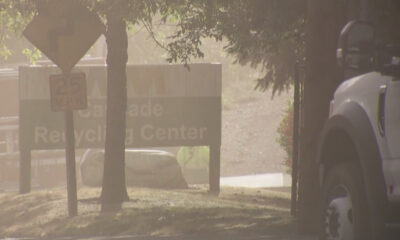 Dusty outdoor scene with a white truck on the right; foreground signs include a 25 mph sign and a 'Recycling Center' sign partially visible behind a tree.