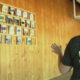Woman in a Darrington Youth Coalition shirt stands before a wall of framed portrait photos mounted on wood panels.