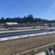 Drag strip with multiple race cars on the track as spectators sit in the bleachers under a clear blue sky.