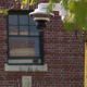 Outdoor dome security camera mounted on a white bracket beside a brick building, monitoring the area outside a window.