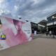 Large pink mural at a shopping center showing an illustrated woman with a colorful bag, outside a store complex including Abercrombie & Fitch.