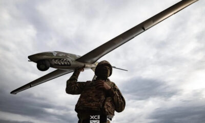 Soldier in camouflage carrying a large winged drone over his shoulder against a cloudy sky