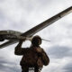 Soldier in camouflage carrying a large winged drone over his shoulder against a cloudy sky