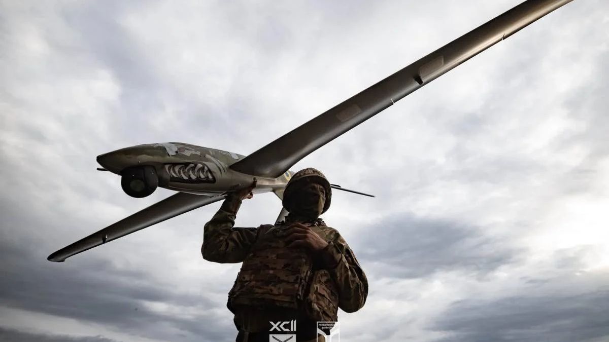 Soldier in camouflage carrying a large winged drone over his shoulder against a cloudy sky