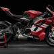Red Ducati sport motorcycle on a rear stand against a black studio backdrop with white accents on the fairings.