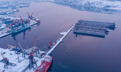 Aerial view of a snow-covered harbor with cranes, ships, and floating docks along a calm riveric waterway of the port.