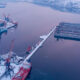 Aerial view of a snow-covered harbor with cranes, ships, and floating docks along a calm riveric waterway of the port.
