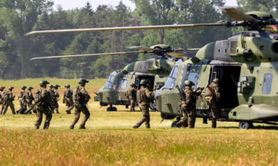 Soldiers in camouflage board a green military helicopter on a grassy airfield.