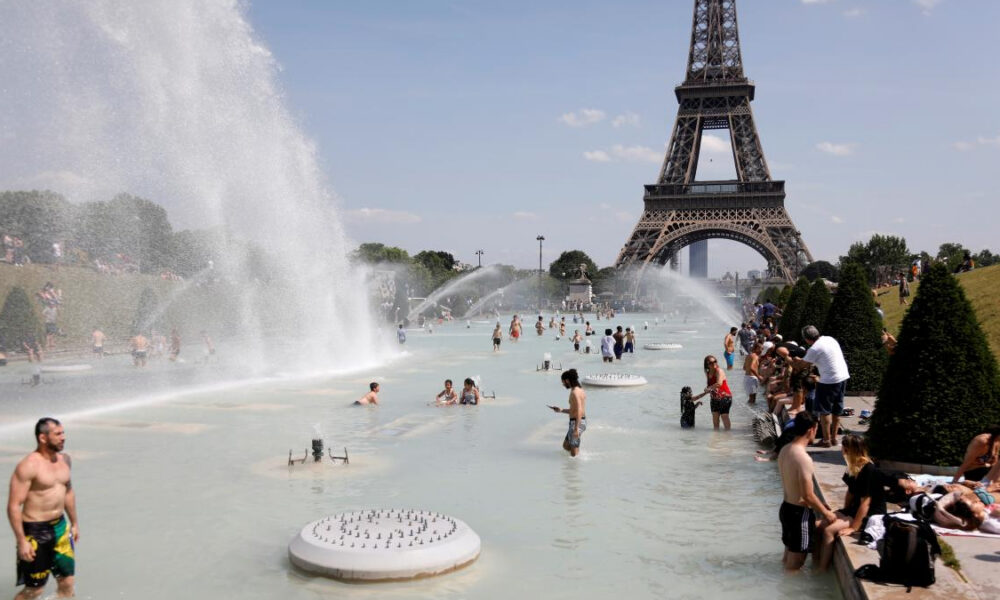 People wading in a large fountain with water jets, Eiffel Tower in the background on a sunny day in Paris tranquilly unfolding the scene nearby parkgoers.