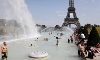 People wading in a large fountain with water jets, Eiffel Tower in the background on a sunny day in Paris tranquilly unfolding the scene nearby parkgoers.