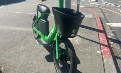Bright green Lime bike with front basket parked at a curb on a city sidewalk (bike-share bicycle).