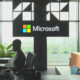 Silhouette of a person working at a curved reception desk in front of a large Microsoft sign with a windowed city view behind.