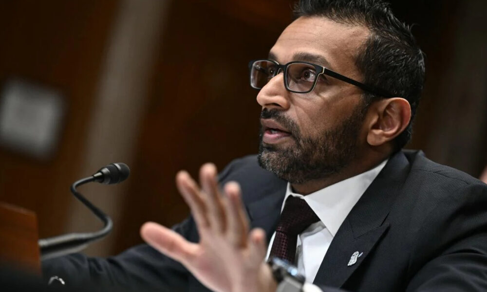Man in a dark suit and glasses speaking into a microphone at a podium in a formal setting.