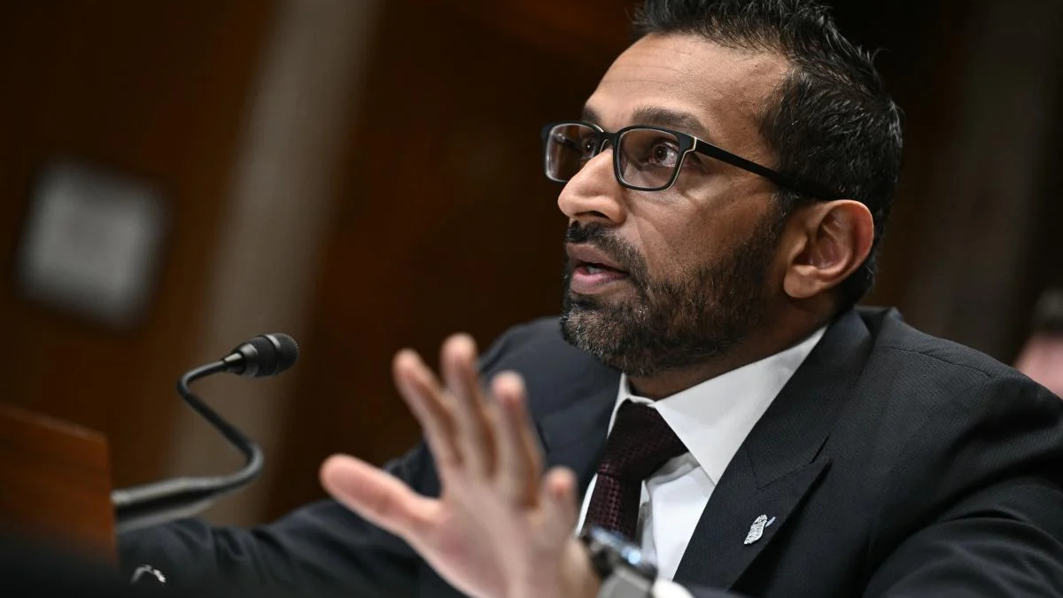 Man in a dark suit and glasses speaking into a microphone at a podium in a formal setting.