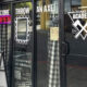 Storefront advertising an axe-throwing venue: glass doors say 'Come Throw An Axe' with a neon 'OPEN' sign and an 'AXE ACADEMY' logo; a sidewalk sign outside sits on brick.