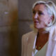 Senior woman with short blonde hair wearing a light blazer and gold pendant necklace, looking to the right.