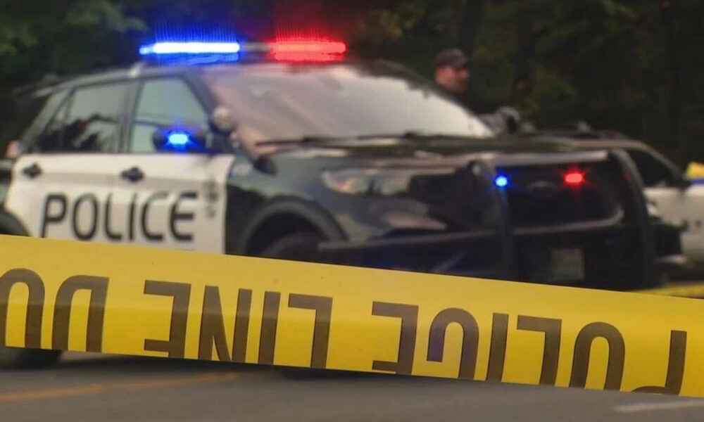 Police car with red and blue lights behind yellow crime scene tape in the foreground.