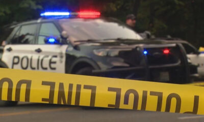 Police car with red and blue lights behind yellow crime scene tape in the foreground.