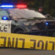 Police car with red and blue lights behind yellow crime scene tape in the foreground.