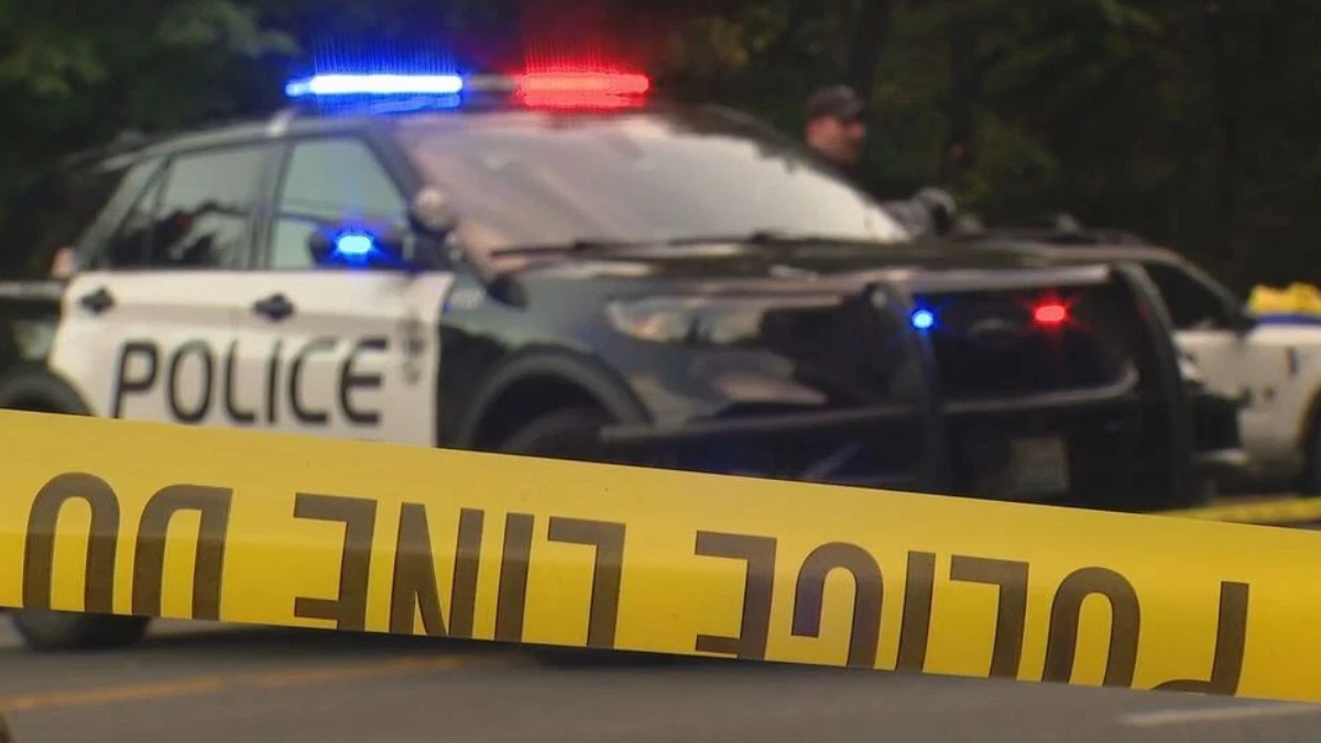 Police car with red and blue lights behind yellow crime scene tape in the foreground.