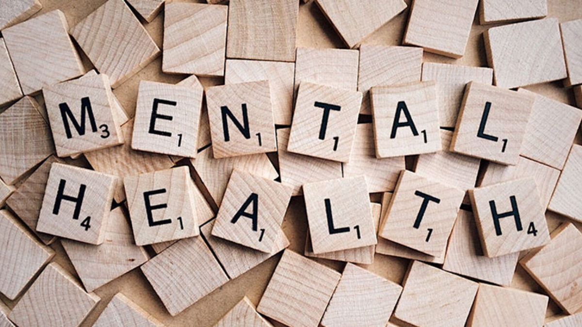Wooden Scrabble tiles spell 'MENTAL HEALTH' on a pale wooden surface.