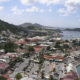 Aerial view of a coastal town built on hills, with colorful red-roofed buildings, a busy waterfront, and a blue bay.