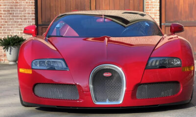Front view of a red Bugatti sports car parked on a driveway with brick walls in the background, showing a distinctive horseshoe grille and sleek headlamps.