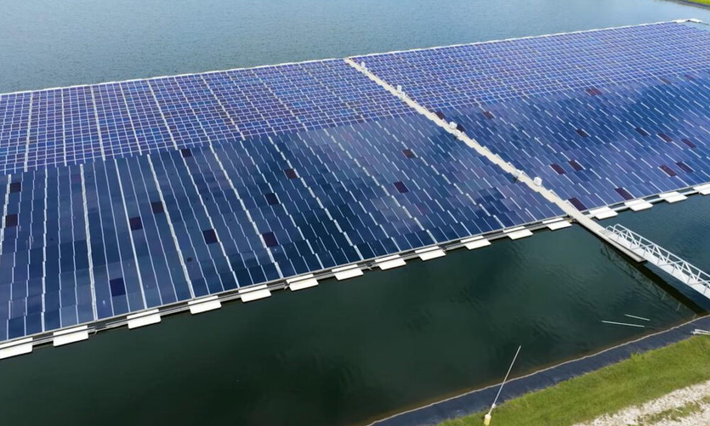 Aerial view of a floating solar farm covering a lake with rows of blue solar panels connected on pontoons.