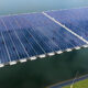 Aerial view of a floating solar farm covering a lake with rows of blue solar panels connected on pontoons.