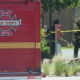 Rear view of a red City of Seattle Fire Department engine with two firefighters behind yellow caution tape in a suburban street.