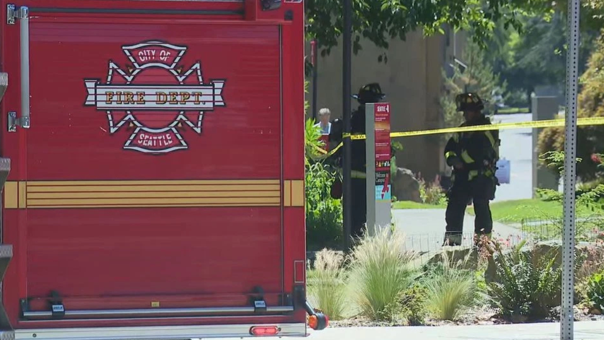 Rear view of a red City of Seattle Fire Department engine with two firefighters behind yellow caution tape in a suburban street.